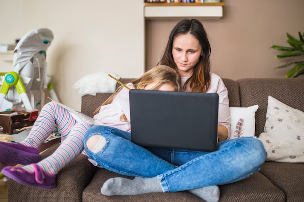 Free photo mother with her daughter sitting on sofa using laptop