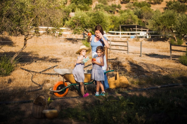 Free Photo mother with her two daughter holding red ripe apple in the field