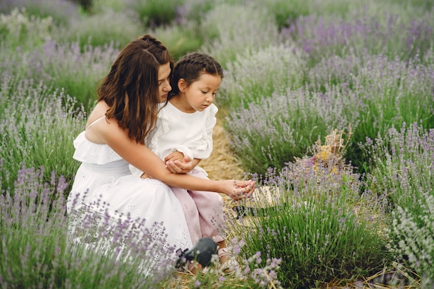 Mother with little daughter on lavender field. Beautiful woman and cute baby playing in meadow field. Family holiday in summer day.