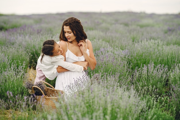 Mother with little daughter on lavender field. Beautiful woman and cute baby playing in meadow field. Family holiday in summer day.