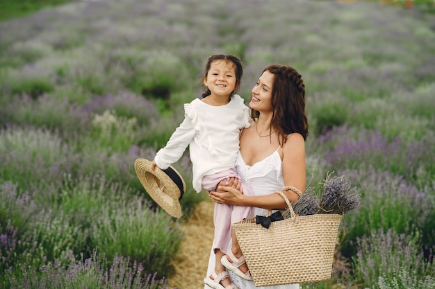 Mother with little daughter on lavender field. Beautiful woman and cute baby playing in meadow field. Family holiday in summer day.