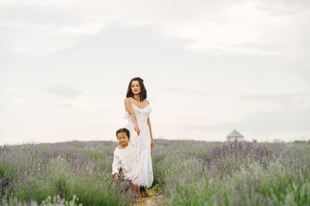 Mother with little daughter on lavender field. Beautiful woman and cute baby playing in meadow field. Family holiday in summer day.