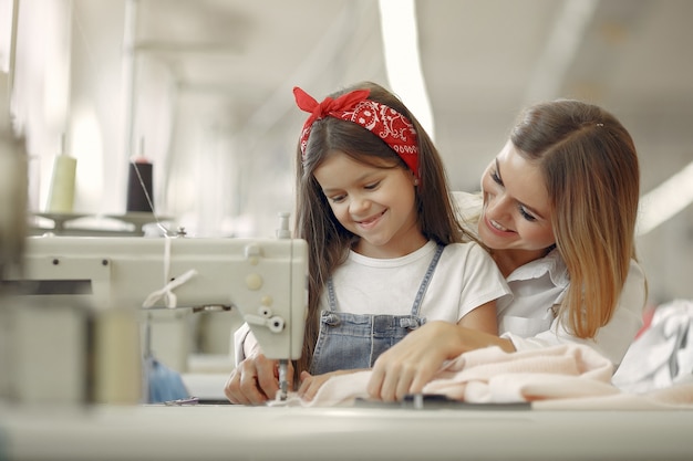 Mother with little daughter sew clothes in the factory