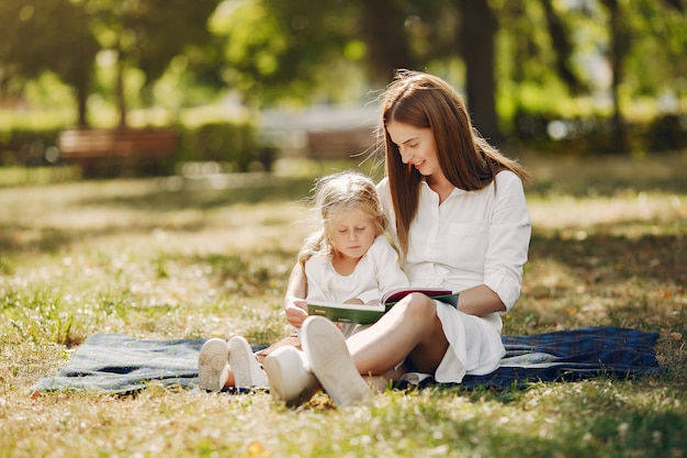 Mother with little daughter sitting on a plaid and read the book