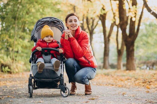 Mother with little son in baby stroller walking in autumnal park