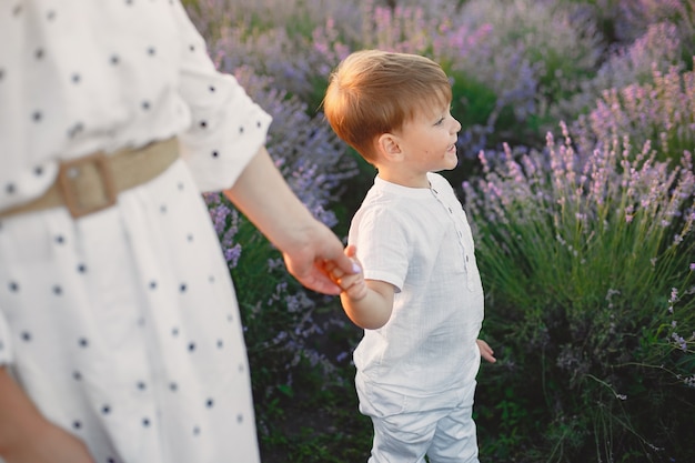 Free photo mother with little son on lavender field. beautiful woman and cute baby playing in meadow field. family holiday in summer day.