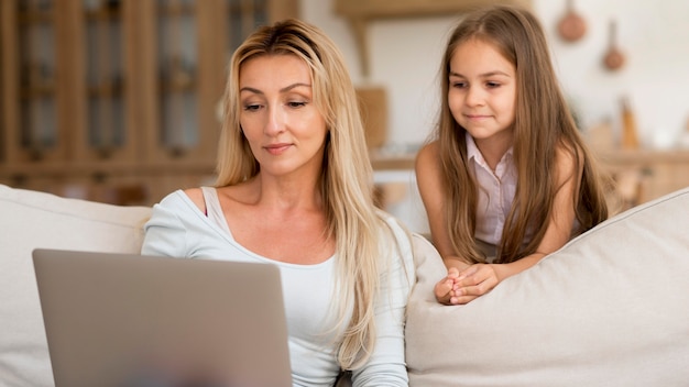 Mother working on laptop from home with daughter watching