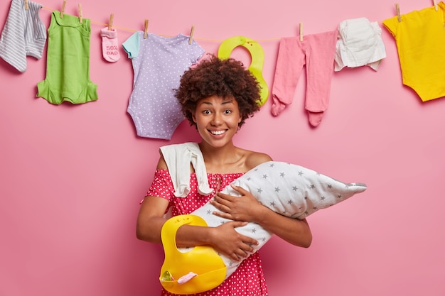 Motherhood, parenthood, child care concept. Happy young mother carries baby on arms, holds bib, poses 