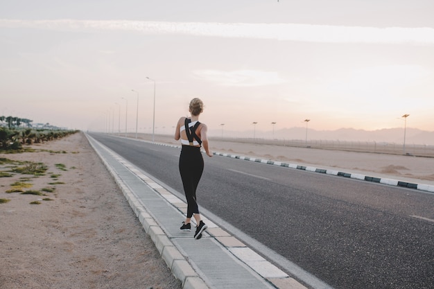 Free photo motivated amazing woman from back running on road in sunny morning. workout, training, true emotions, healthy lifestyle, hardworking, strong sportswoman, tropical country.