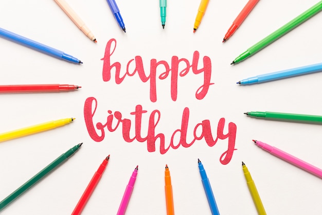 Free photo motivational phrase 'happy birthday' for greeting cards and posters drawing with red marker on white paper. lettering on paper between colourful markers