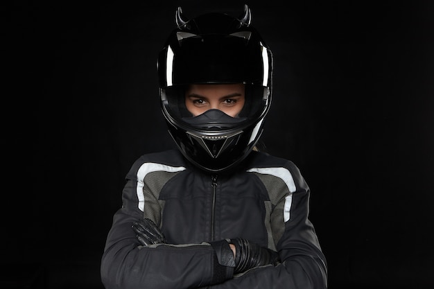 Motorcycle sports, extreme, competition and adrenaline. Active young female racer wearing protective helmet and uniform going to participate in road racing or motorcross, crossing arms on her chest