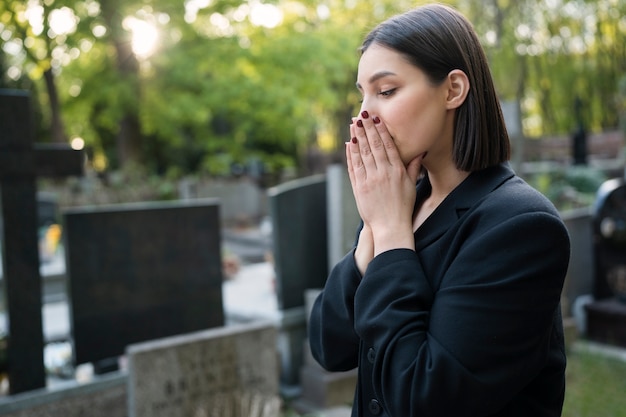 Mourning woman praying next to grave at the cemetery