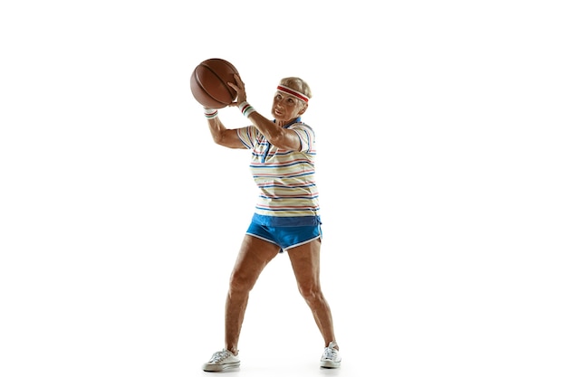 Move. Senior woman wearing sportwear playing basketball on white background. Caucasian female model in great shape stays active. Concept of sport, activity, movement, wellbeing, confidence. Copyspace.