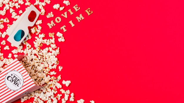 Movie time text with 3d glasses and spilled popcorn on red background