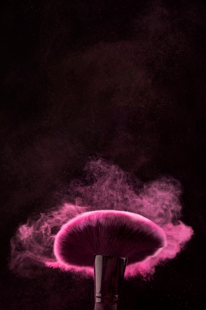 Free photo moving brush in cloud of makeup powder on black background