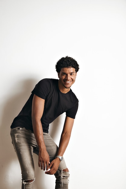 Free Photo moving playful athletic black model with an afro wearing a blank black t-shirt and grey skinny jeans on white wall