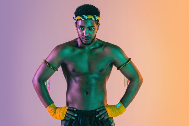 Muay thai. Young man exercising thai boxing on gradient background in neon light.