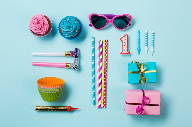 Muffins; sunglasses; party horn blowers; drinking straws; candle and gift boxes; sparkler on blue backdrop