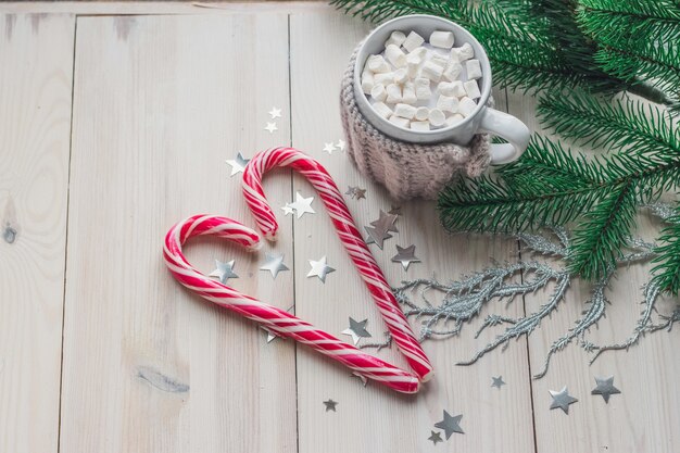 Mug of marshmallows and candy canes surrounded by Christmas decorations on a wooden table