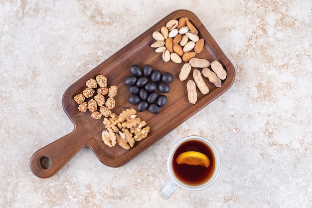 Mug of tea next to a snack serving with small piles of nuts and candy on a board 