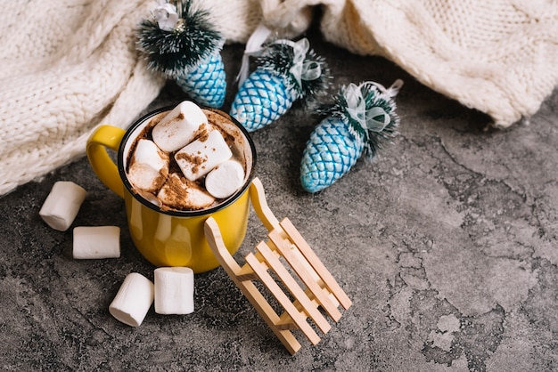 Free photo mug with marshmallows near christmas toys and sweater