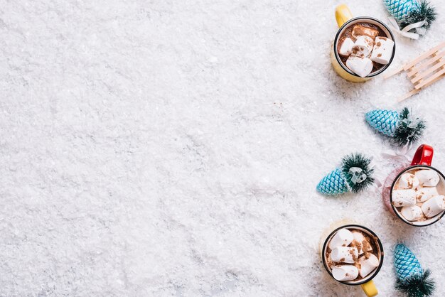 Mugs with marshmallows and drinks near Christmas toys between snow