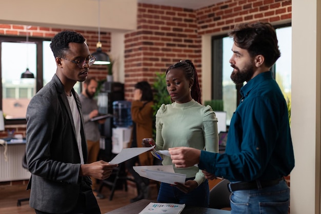 Free photo multi-ethnic businesspeople discussing business collaboration after analyzing marketing statistics. freelancer woman explaining company strategy working at financial project in brick wall office