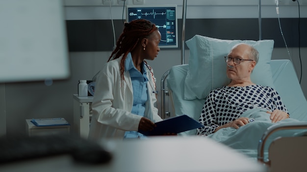 Free photo multi ethnic medical staff explaining disease to patient in hospital ward bed at clinic sick old man...