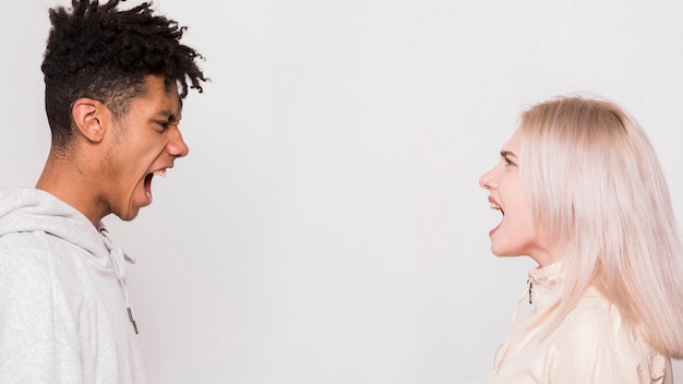 Multi ethnic young couple standing face to face screaming against whit background