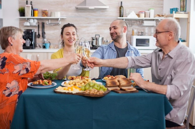 Free photo multi generation family toasting with white wine during lunch. tasty seasoned potatoes. senior parents. delicious grapes.