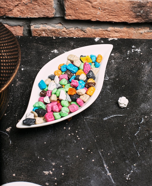 Multicolor bonbon sweets (ball candies) inside white plate bowl on stone brick