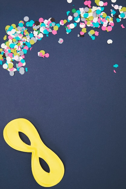 Free Photo multicolored confetti with yellow eye mask on colored background