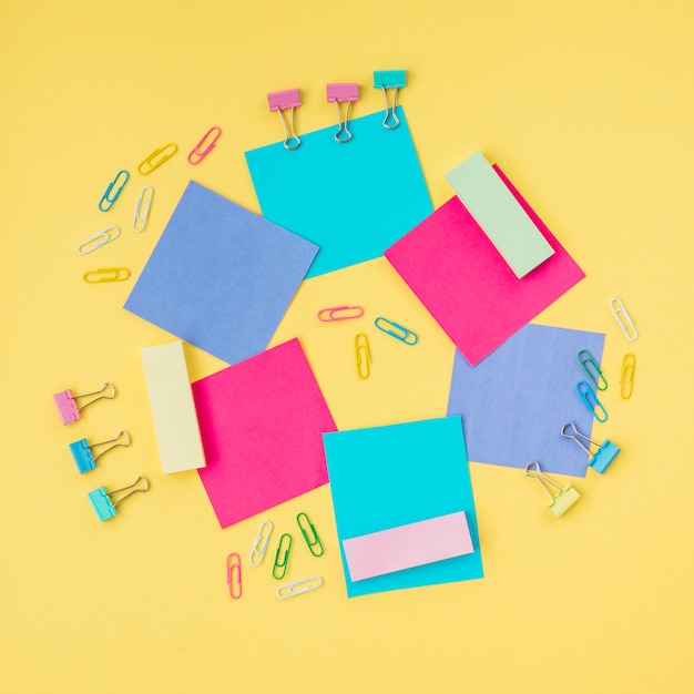 Free photo multicolored sticky notes and paper clip on yellow surface