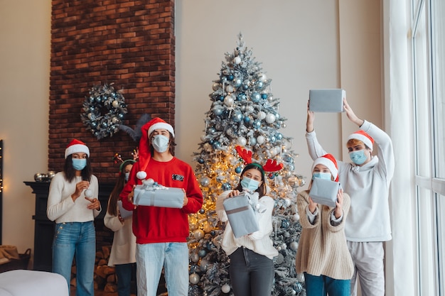 Multiethnic group of friends in Santa hats smiling and posing with gifts in hands