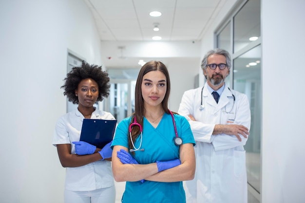 Free photo a multiethnic group of three doctors and nurses standing in a hospital corridor wearing scrubs and coats the team of healthcare workers are staring at the camera and smiling