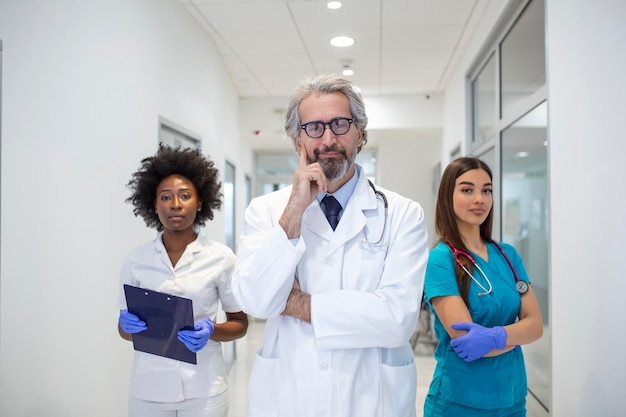 A multiethnic group of three doctors and nurses standing in a hospital corridor wearing scrubs and coats The team of healthcare workers are staring at the camera and smiling