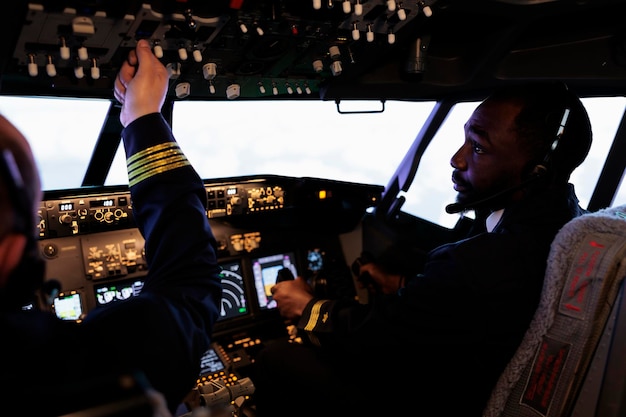 Free photo multiethnic team of pilots using control panel in cockpit to fly airplane, pushing power switch and dashboard command buttons to takeoff. international airways service with aircrew in cabin.