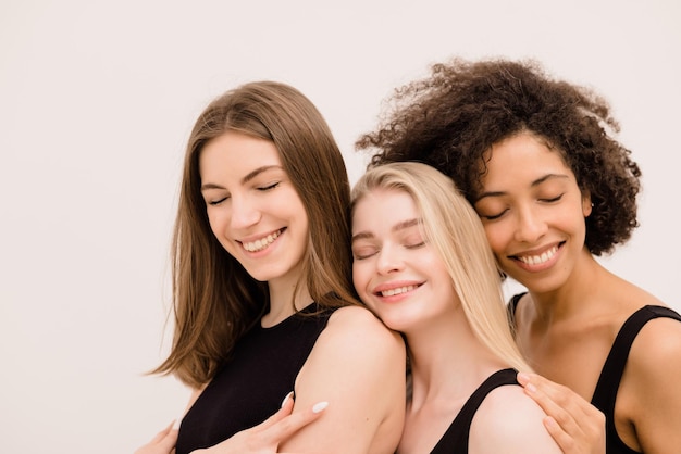 Free photo multiethnic young three women models with closed eyes in black tops standing together on white background