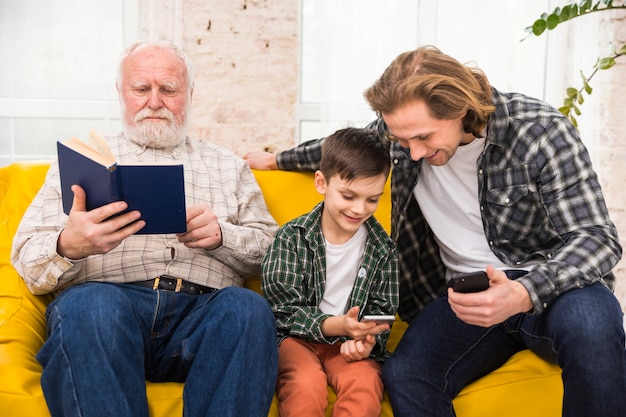 Free Photo multigenerational men spending time together browsing book and smartphones 