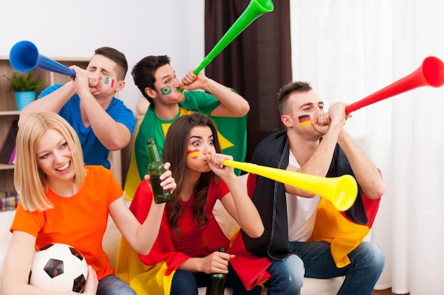 Free photo multinational friends blowing by vuvuzela during the football match