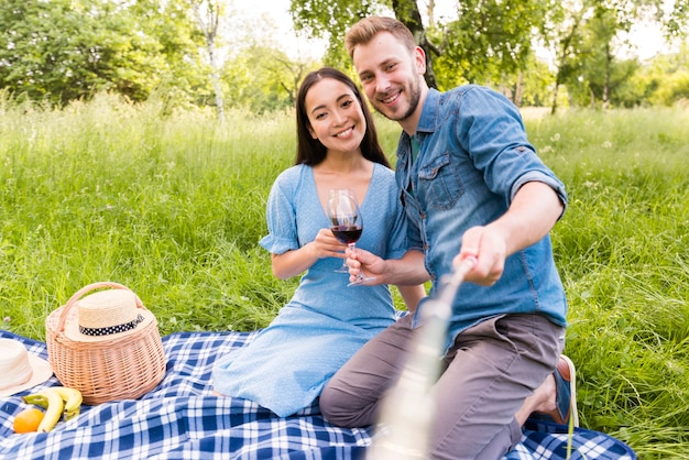 Free photo multiracial adult couple sitting taking selfie with stick