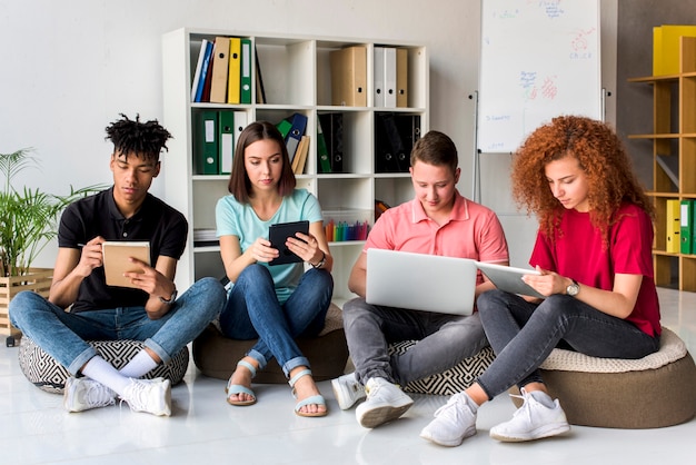 Multiracial friends studying with electronic gadgets and books sitting in study room