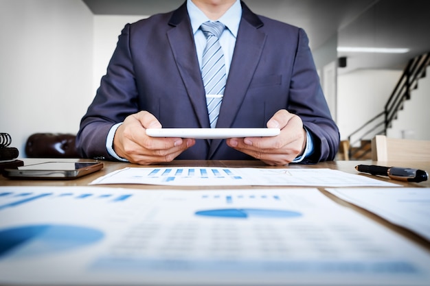 Free Photo multitasking. handsome young man working with touchpad while sitting on the couch in office and financial statistic graph.