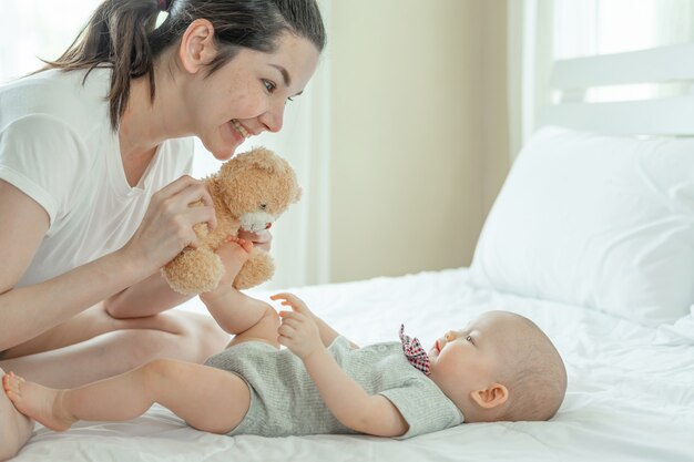 Mum and baby happily tease each other on a white bed.