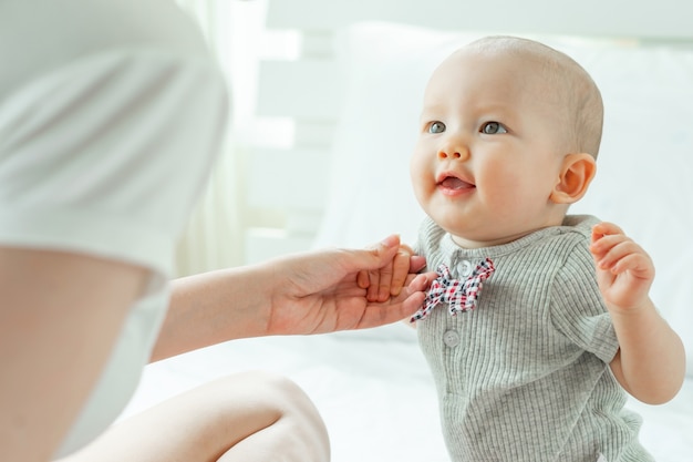 Mum and baby happily tease each other on a white bed.