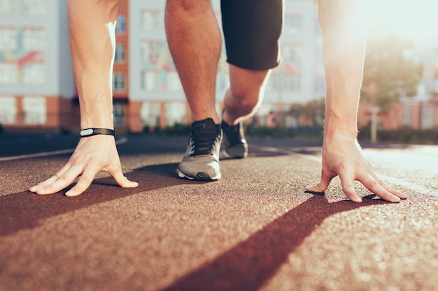 Free photo muscle, hands, sunlight, legs in sneakers of strong guy on stadium in the morning. he has preparation on start.