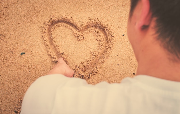 Free photo muscle man draw heart on sand. international sun light and vintage tone.