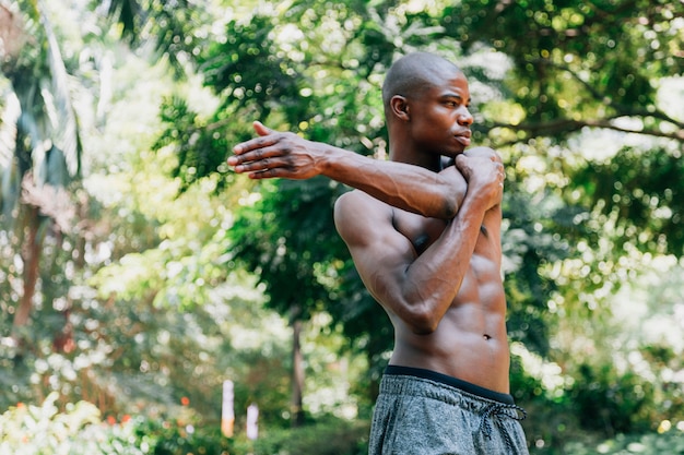 Muscular athlete young man stretching his hand standing in front of trees