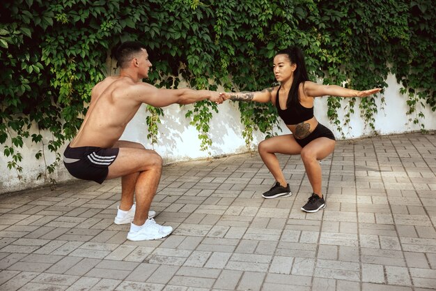 A muscular athletes doing workout at the park. Gymnastics, training, fitness workout flexibility. Summer city in sunny day on background field. Active and healthy lifestyle, youth, bodybuilding.