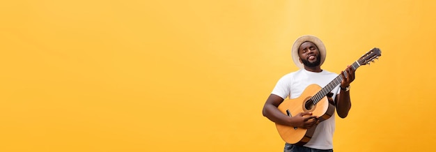 Free photo muscular black man playing guitar wearing jeans and white tanktop isolate over yellow background